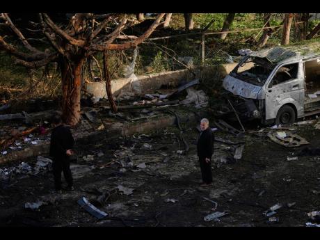 People stand near a damaged van beside scattered debris following an Israeli strike in Beirut, Lebanon.