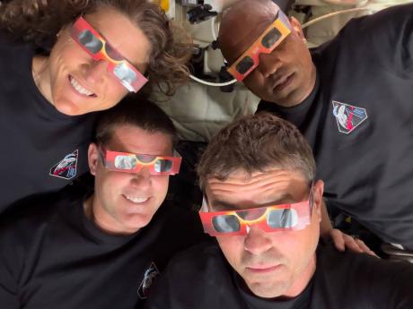 In this image provided by NASA, the Artemis II crew (counterclockwise, from top left), Mission Specialist Christina Koch, Mission Specialist Jeremy Hansen, Commander Reid Wiseman, and Pilot Victor Glover pose with eclipse viewers during a lunar flyby on Ap